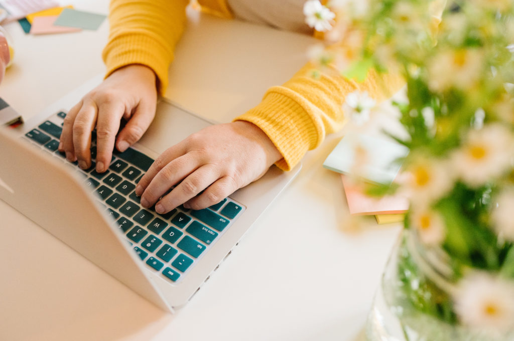 Small business owner working on her DIY website design on mac laptop with teal keyboard cover. 